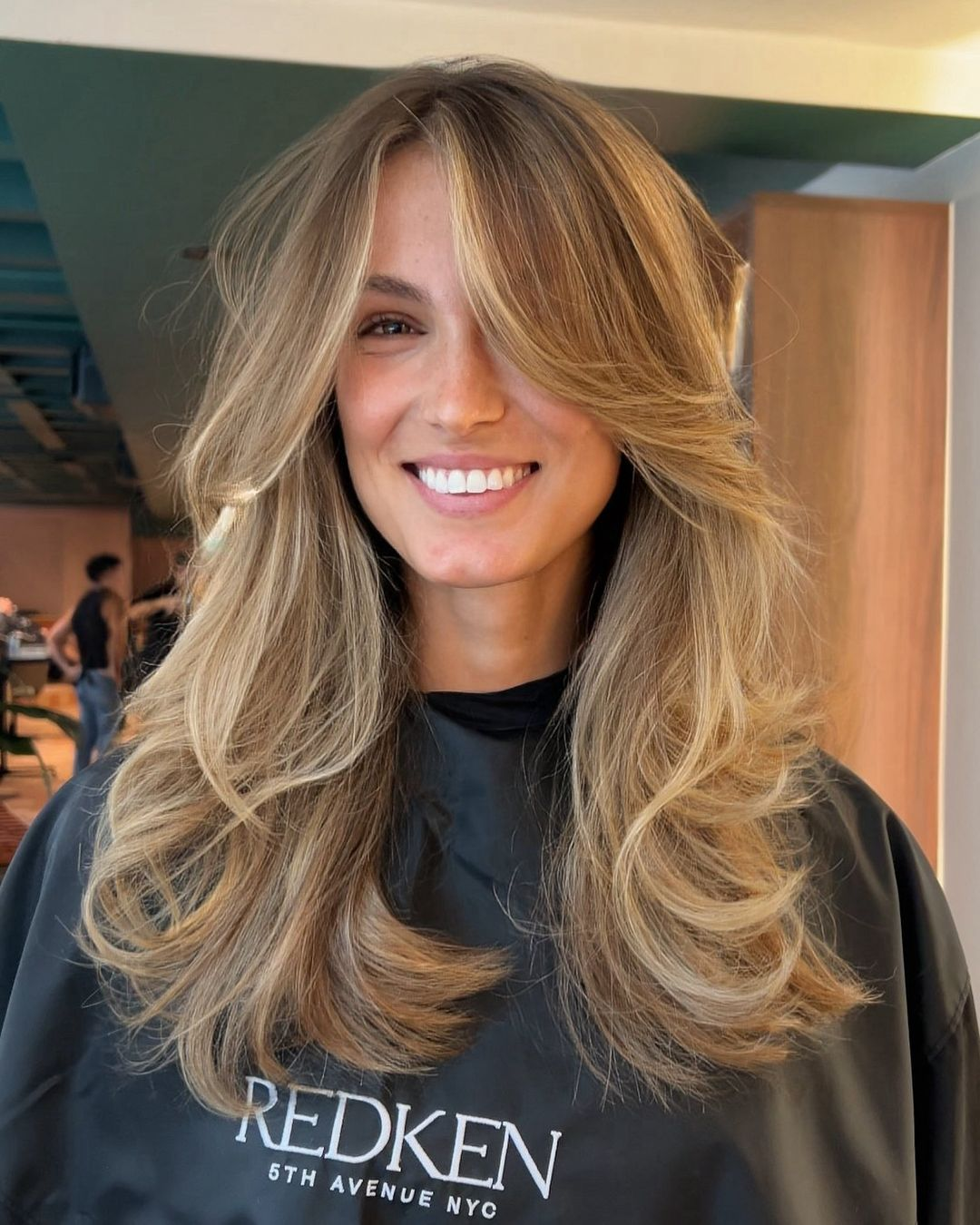 Person with styled hair wearing a Redken cape indoors