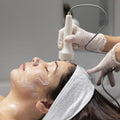 Person receiving a facial treatment with a device on a neutral background