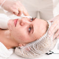 Person receiving a facial treatment with gloved hands applying product to face.