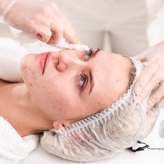 Person receiving a facial treatment with gloved hands applying product to face.