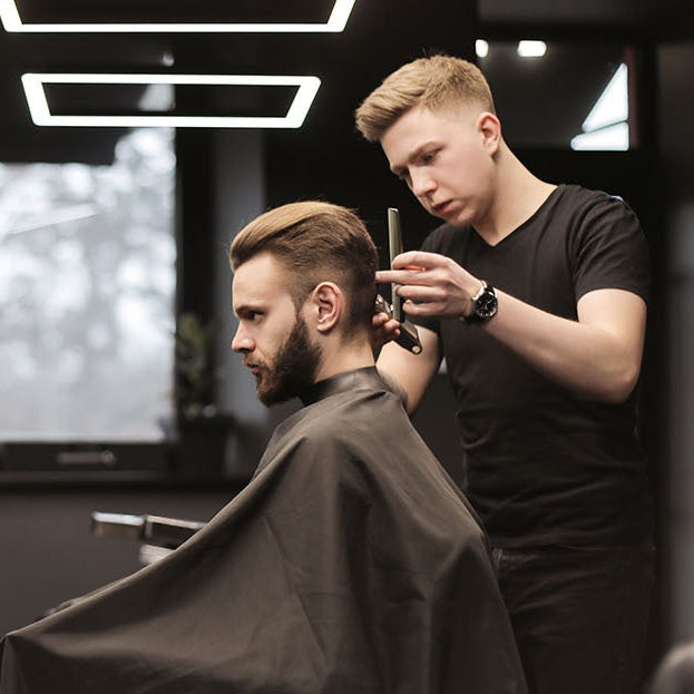 Barber cutting a customer's hair in a well-lit barbershop.