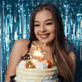 Woman holding a cake with a lit candle against a blue tinsel background