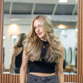Woman with long blonde hair wearing a black crop top and high-waisted jeans standing in front of a mirror.