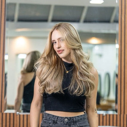 Woman with long blonde hair wearing a black crop top and high-waisted jeans standing in front of a mirror.