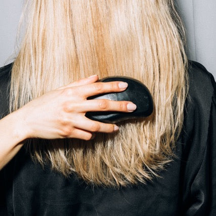 Person with blonde hair using a black hairbrush against a neutral background
