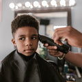 Child getting a haircut in a barbershop with a barber using clippers.