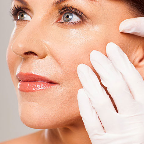 Woman's face being examined by a gloved hand against a neutral background